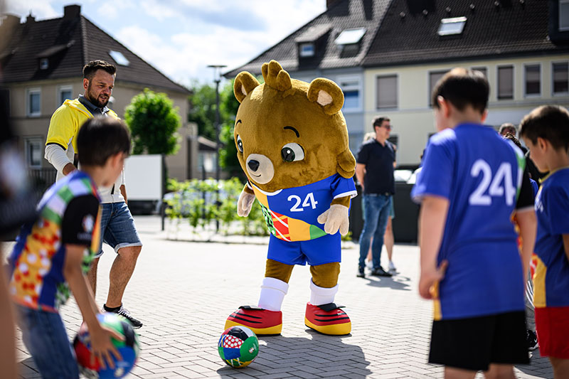 European Championship mascot plays football with children in the street