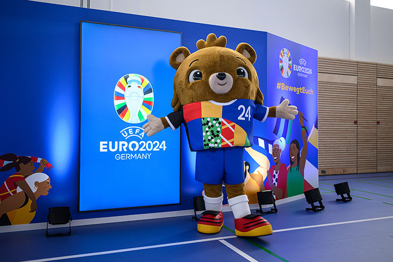 The European Championship mascot poses in front of the logo